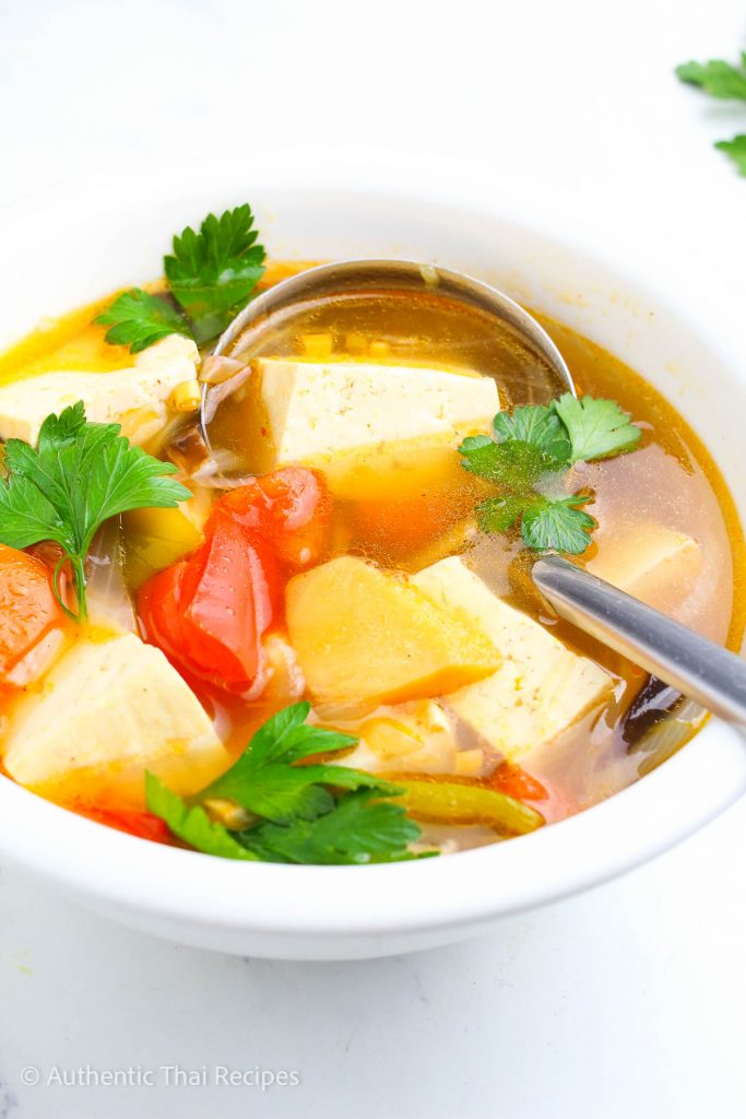 a bowl of the lemongrass soup recipe thai garnished with fresh cilantro with a ladle on it on a white table