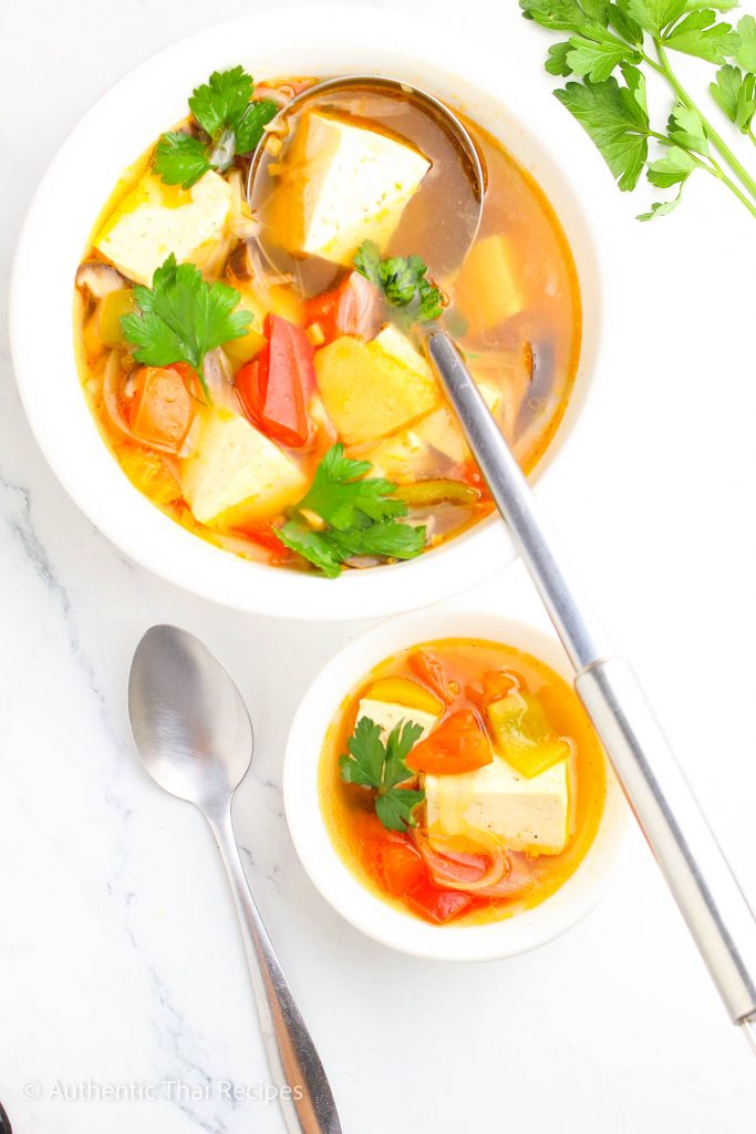 one large bowl of lemongrass soup with a ladle and one small bowl with a spoon beside it on a white table