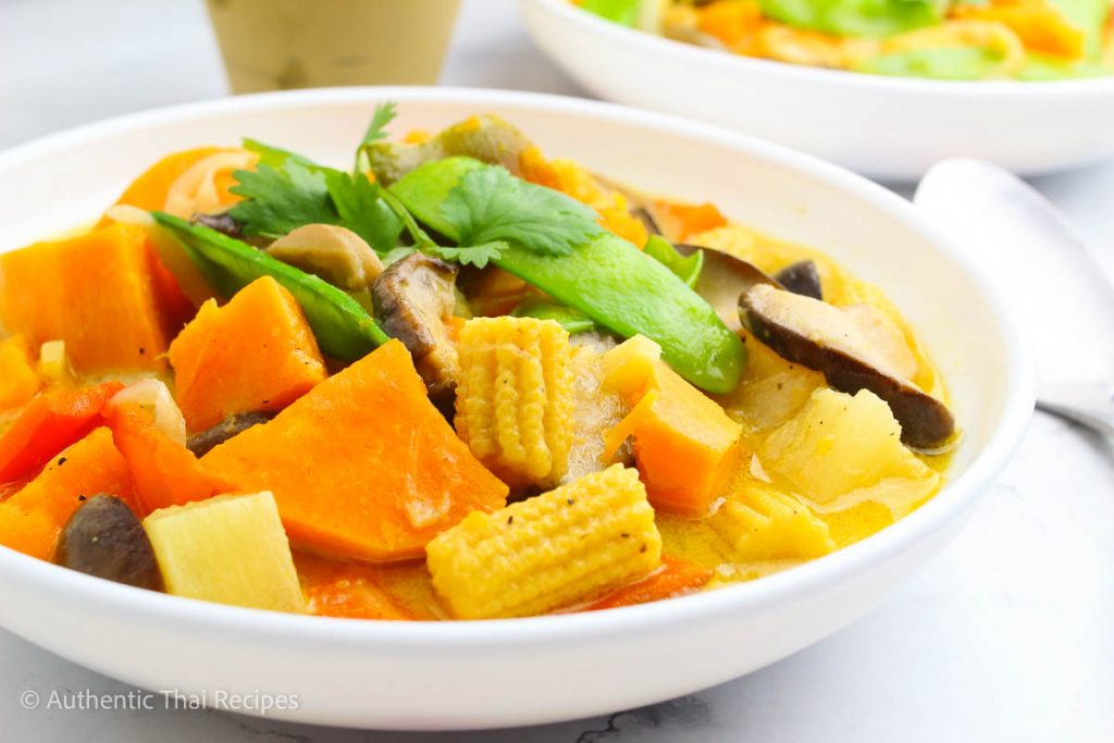 vegan thai green curry in a white bowl topped with a cilantro on a white table