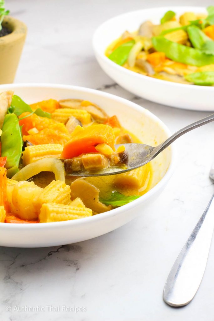 Tasting the vegetable green curry using a spoon served in a bowl on a white table