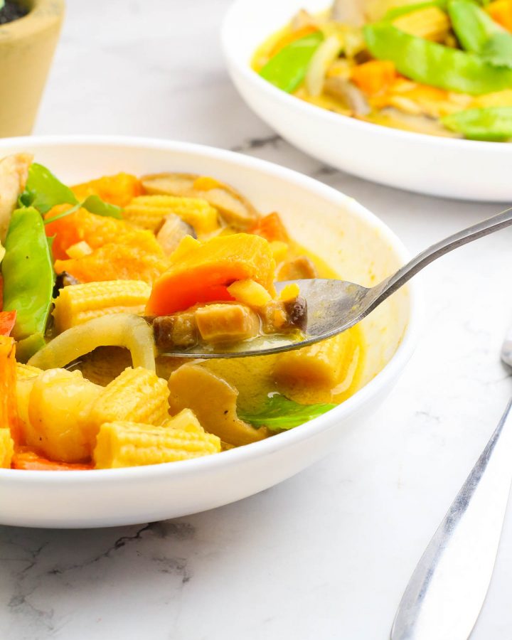 tasting a bowl of thai vegetable green curry using a spoon on a white table