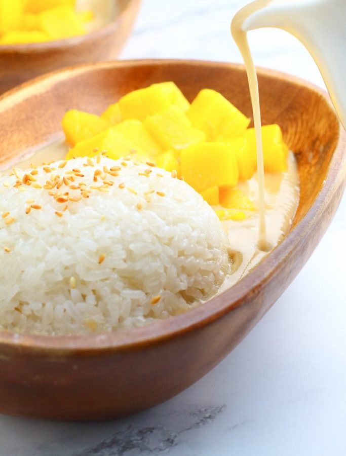 Rice Pudding with ripe mango on the side in a wooden plate with a drip of coconut milk
